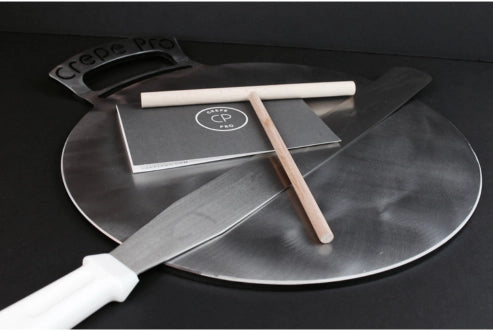 Crepé Pro pizza peel with a knife and rolling pin on a black background. Carbon steel pan crepe pan cooking crepes on stovetop